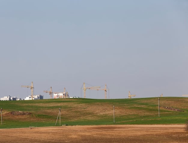 A large wind farm in a rural area, featuring rows of towering wind turbines against a blue sky. The turbines are actively generating electricity, showcasing renewable energy production. The landscape includes rolling hills and open fields.
